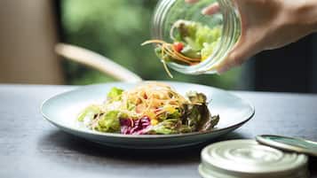 Une main versant une salade dans une assiette.