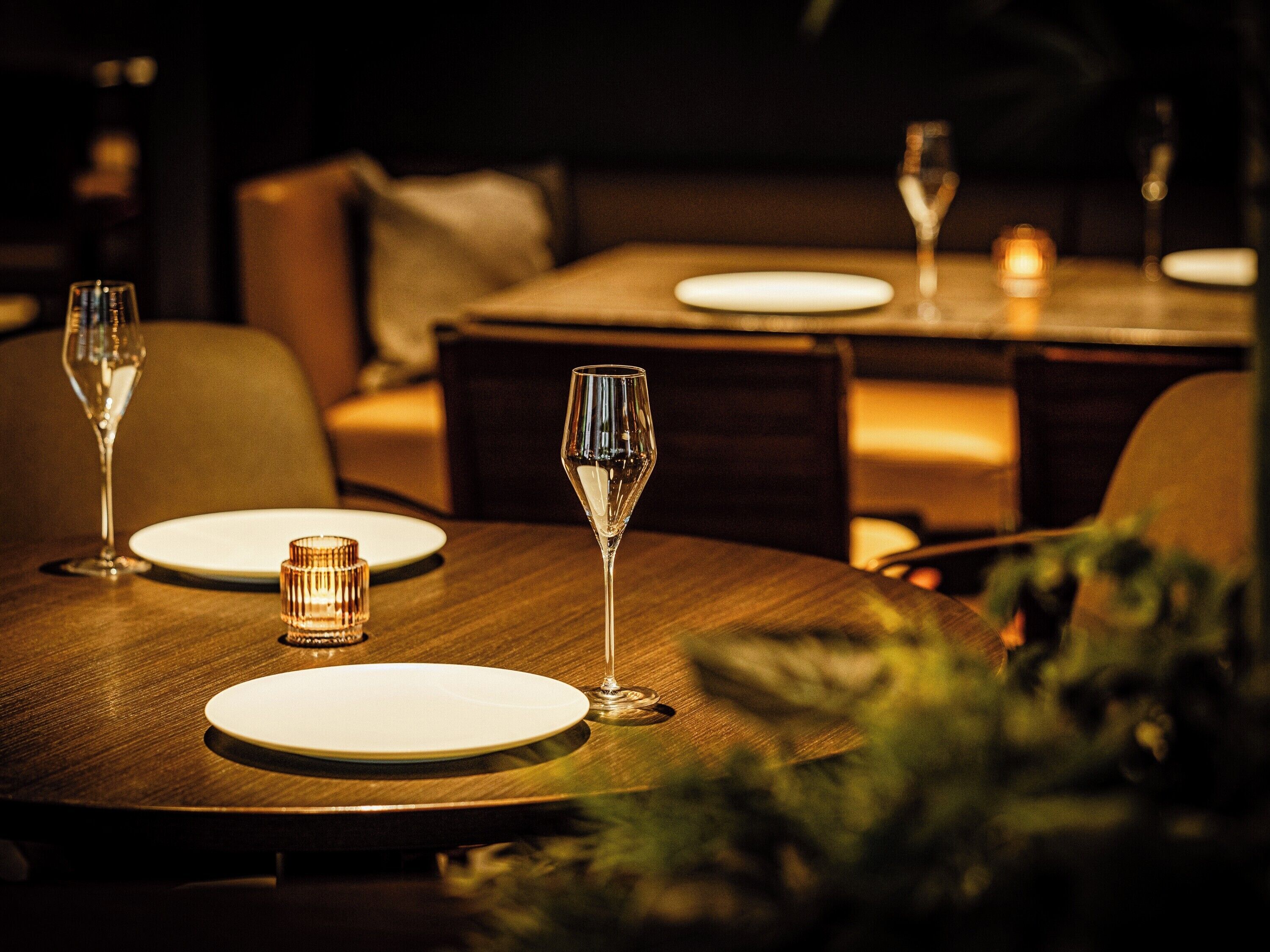A dining table with two wine glasses and a candle, surrounded by chairs and a sofa.