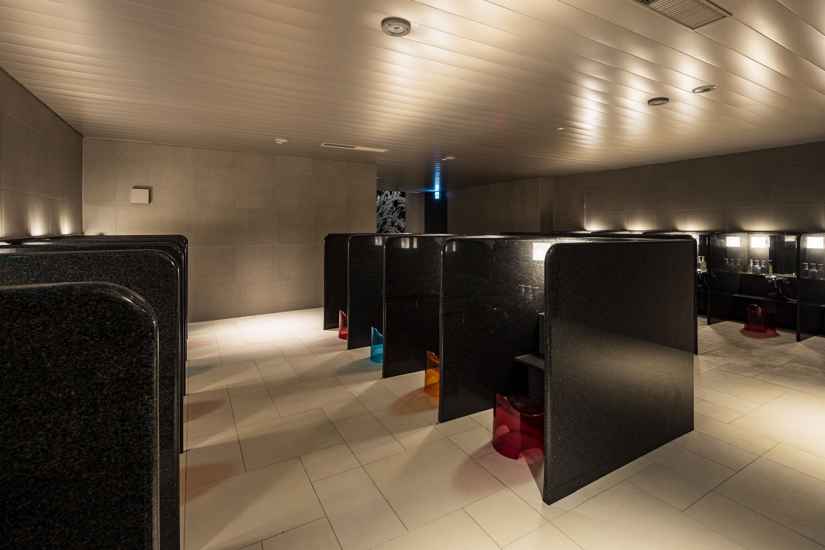 Des toilettes modernes avec des cloisons noires, un sol carrelé et un plafond doté d’un éclairage encastré.