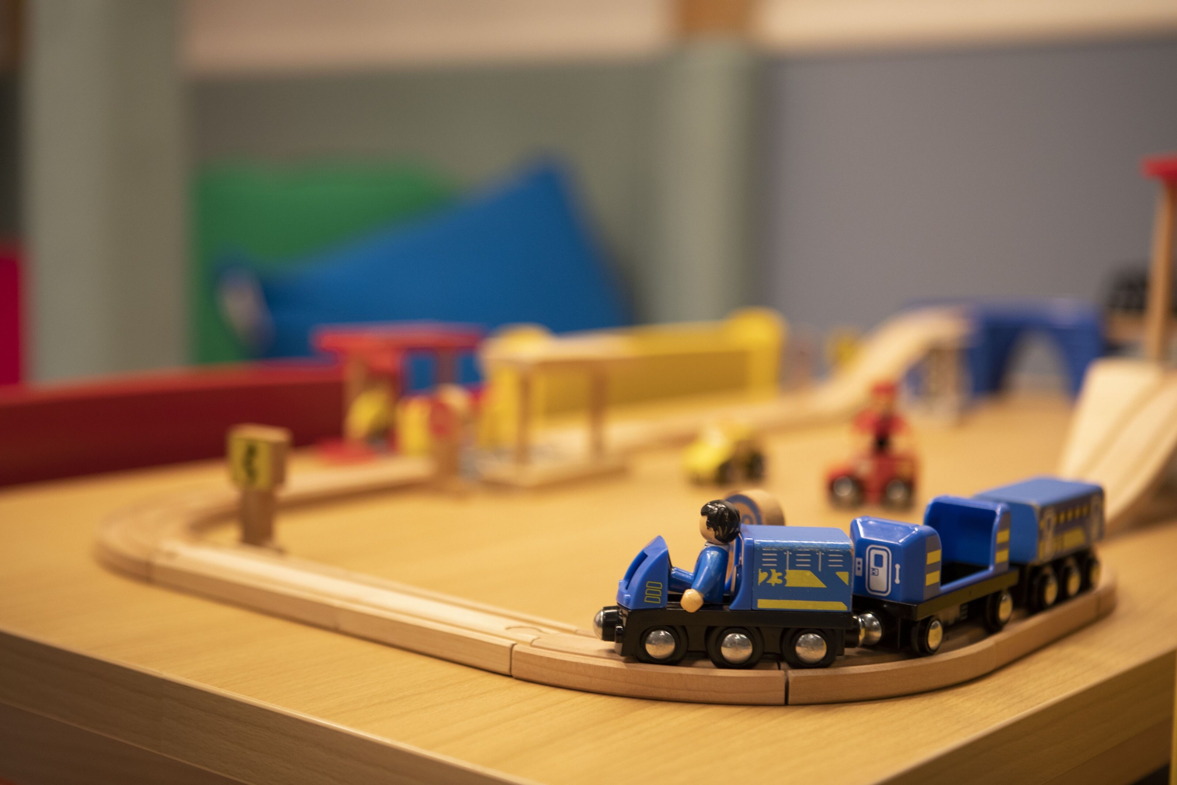 Un juego de trenes modelo con una locomotora azul y vagones, sobre una vía de madera.