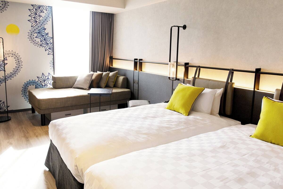 A hotel room with two beds, a sofa, and a desk.