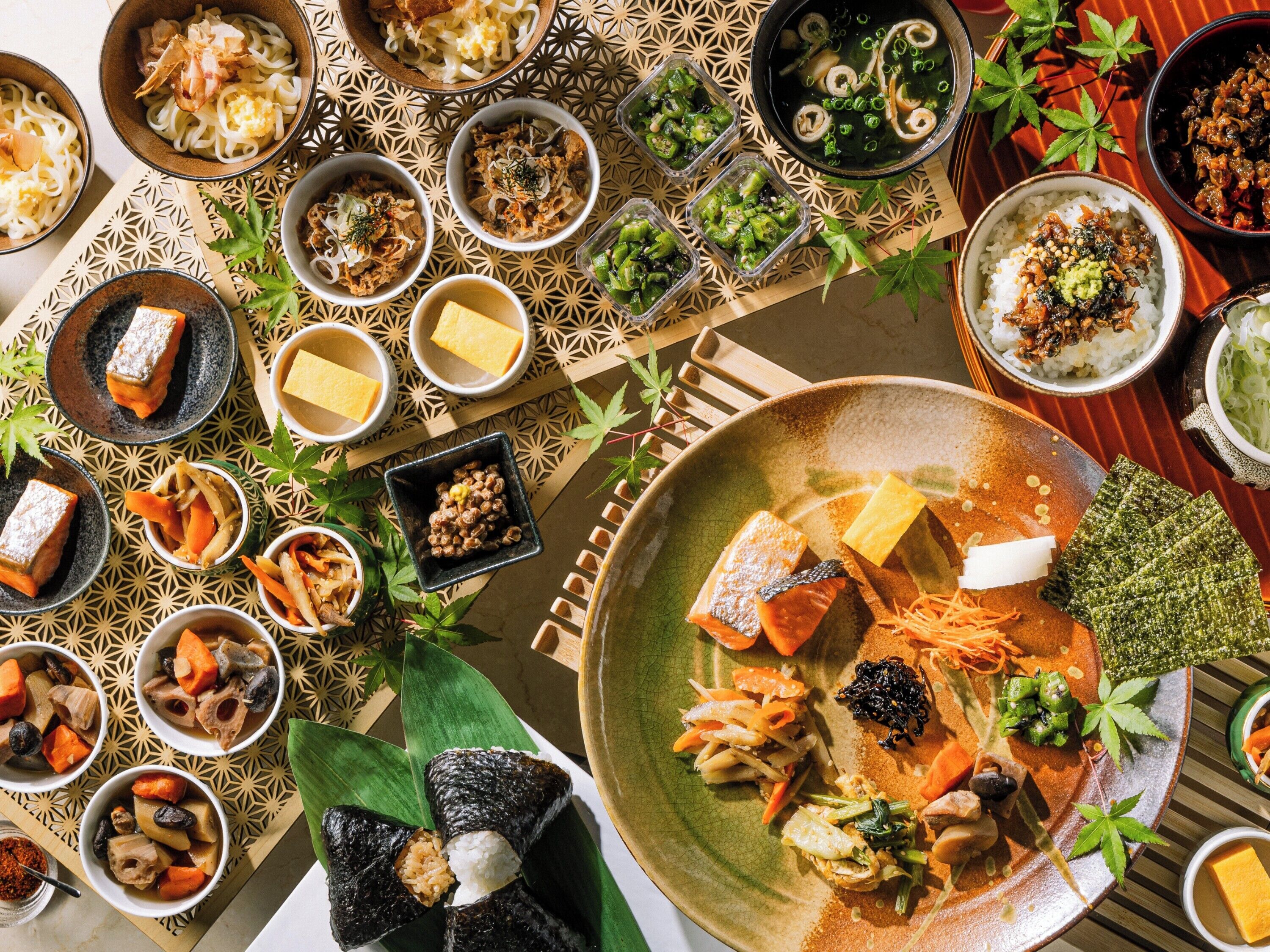 Une variété de plats, notamment des sushis, des sashimis et des bols de riz, présentés sur une table agrémentée d’un motif décoratif.