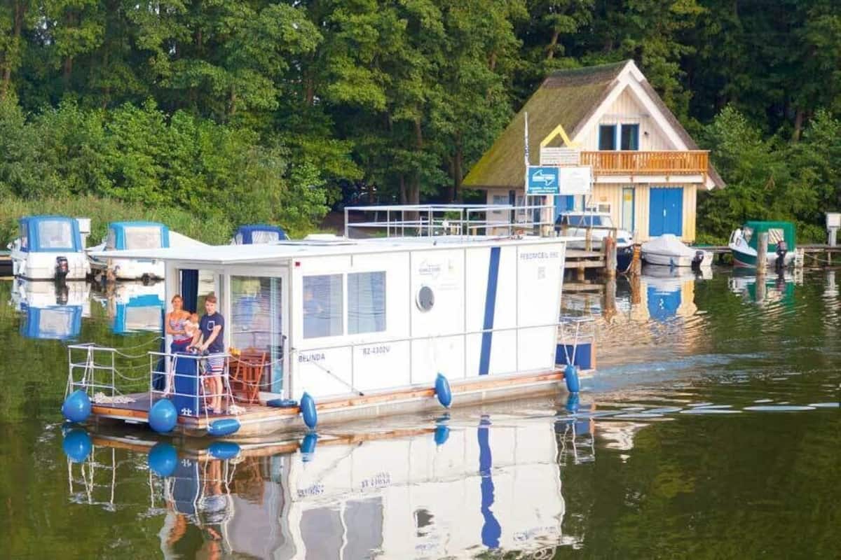 A houseboat docked at a pier with a small deck and a covered area.