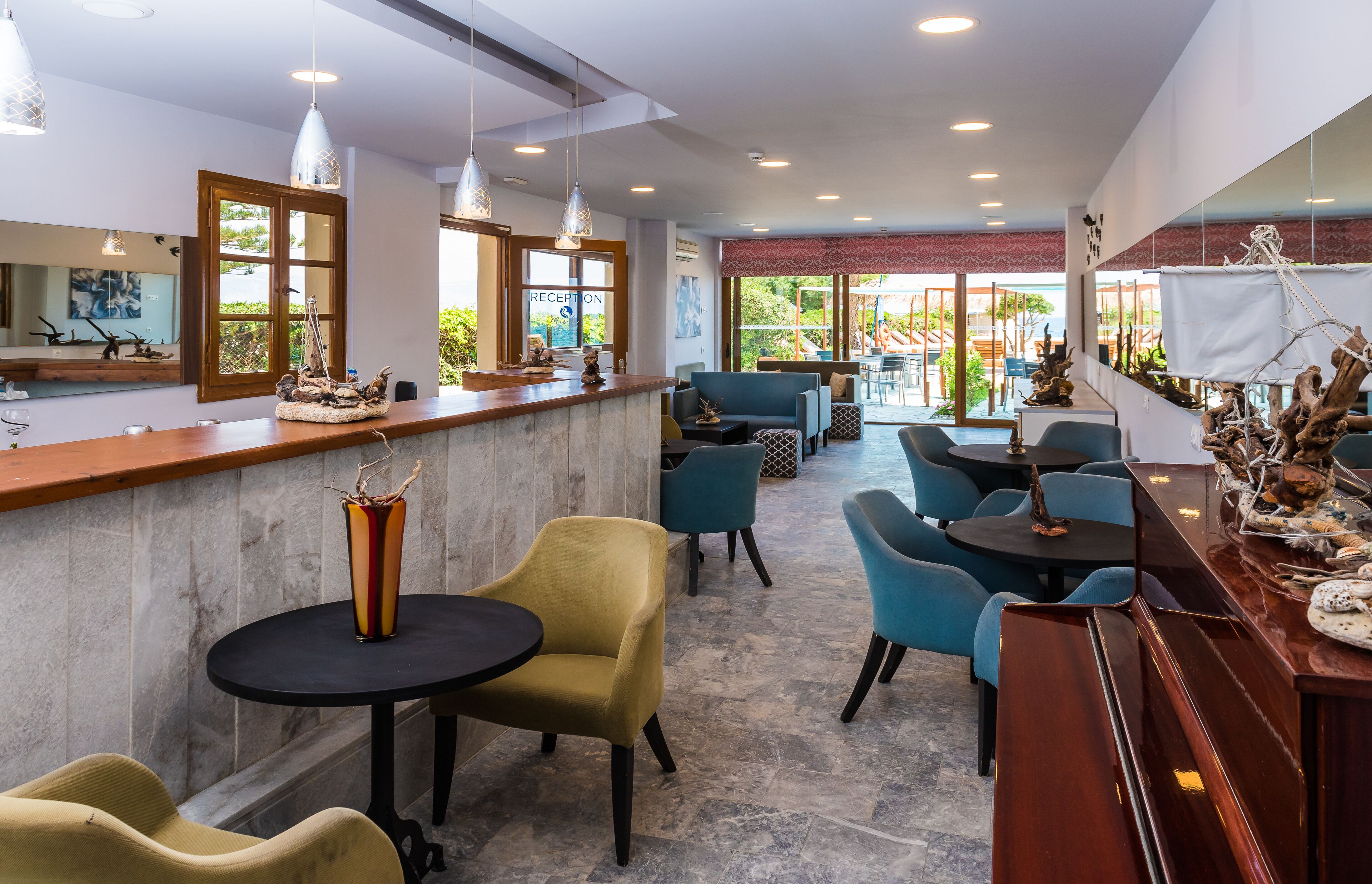 A modern hotel lobby with a reception desk, seating area, and large windows offering a view of the outdoors.
