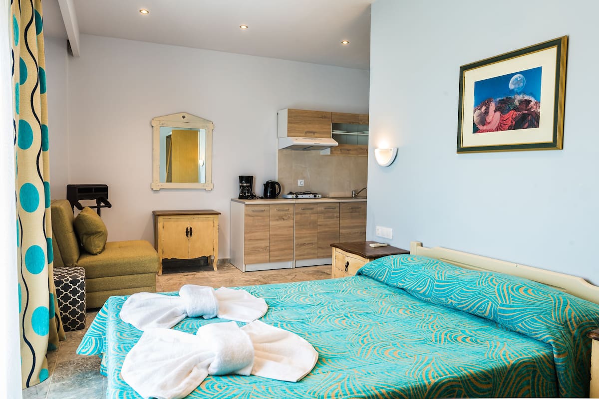 Quarto de hotel com cama, pequena cozinha, banheiro e área de refeições.