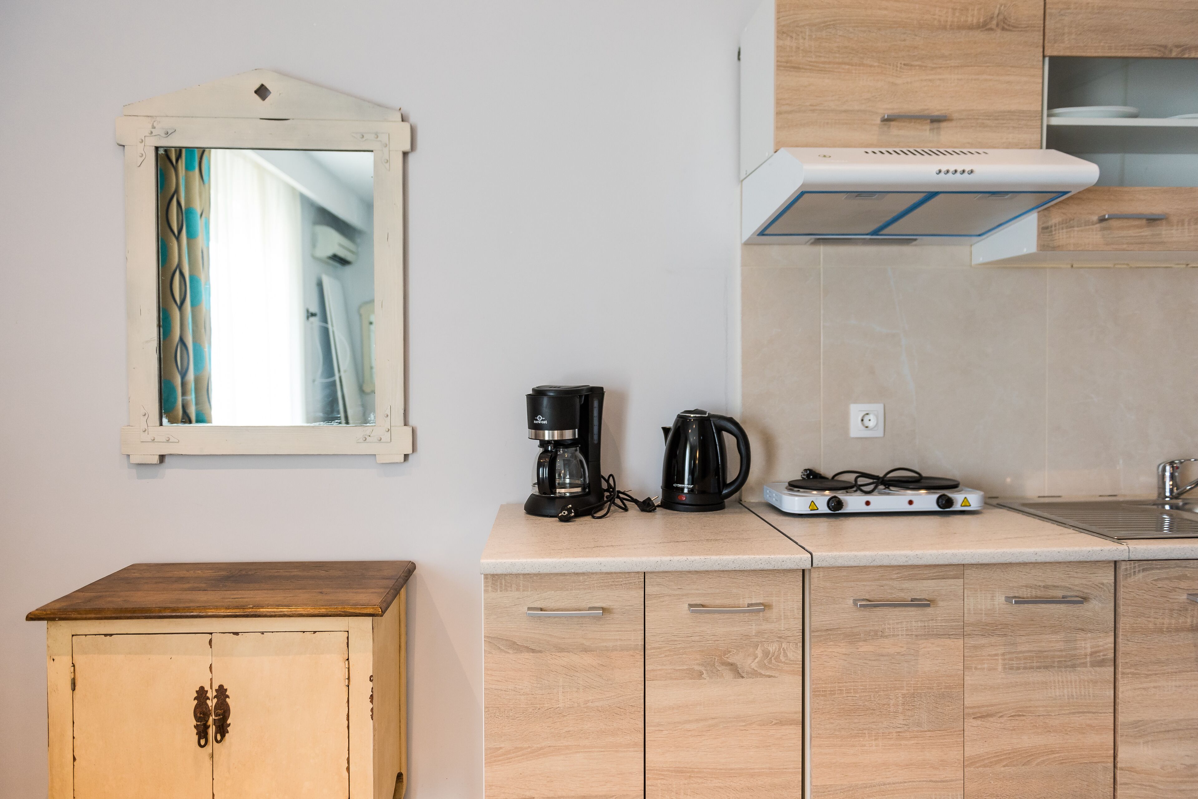 A compact kitchen with a wooden cabinet, a coffee maker, a kettle, and a stove.
