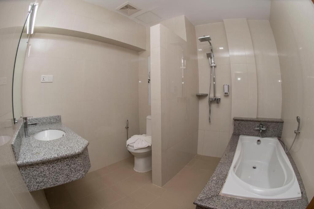 A modern bathroom with a granite countertop sink, a white toilet, a shower area, and a bathtub.