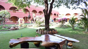 Un patio con una gran mesa de madera, un árbol y un edificio con ventanas arqueadas al fondo.