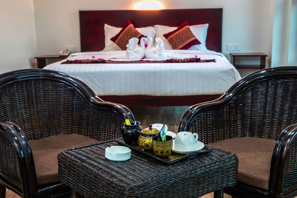 Habitación de hotel con cama, dos sillones de mimbre, una bandeja con juego de té y mesita de noche con teléfono.