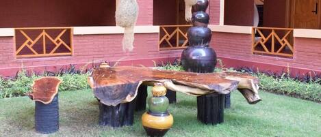 Um pátio com mesa de madeira, vasos e decorações pendentes, com uma parede de tijolos vermelhos e janelas arqueadas.
