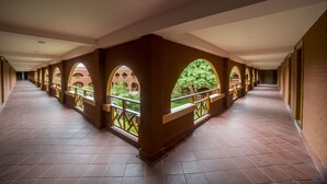 Un pasillo con arcos y piso de baldosas que conduce a un patio con árboles.