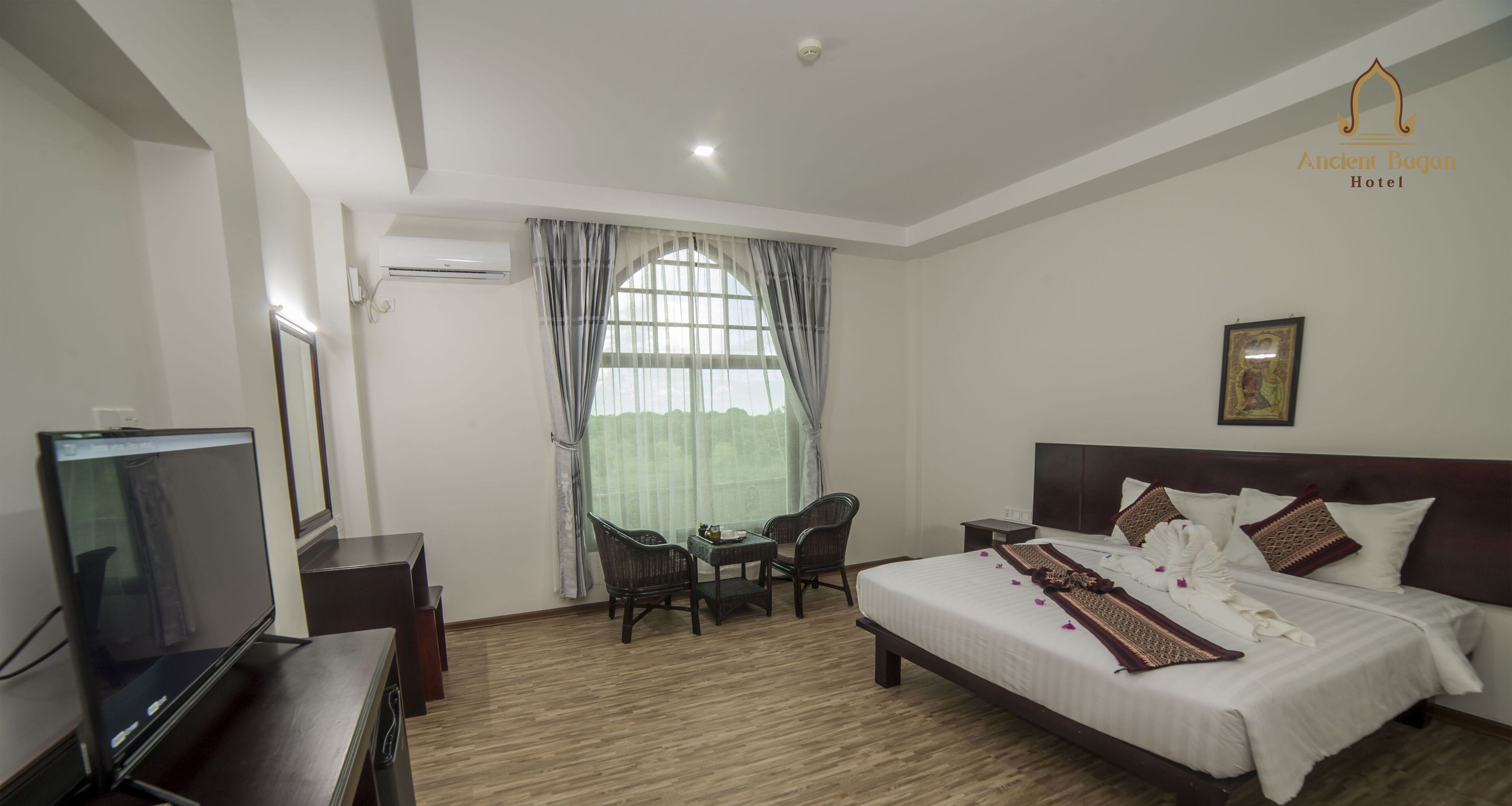 A hotel room with a bed, a television, a desk, and a window with curtains.