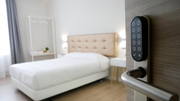 Ett modernt hotellrum med en säng, ett nattduksbord och en väggmonterad kontrollpanel.