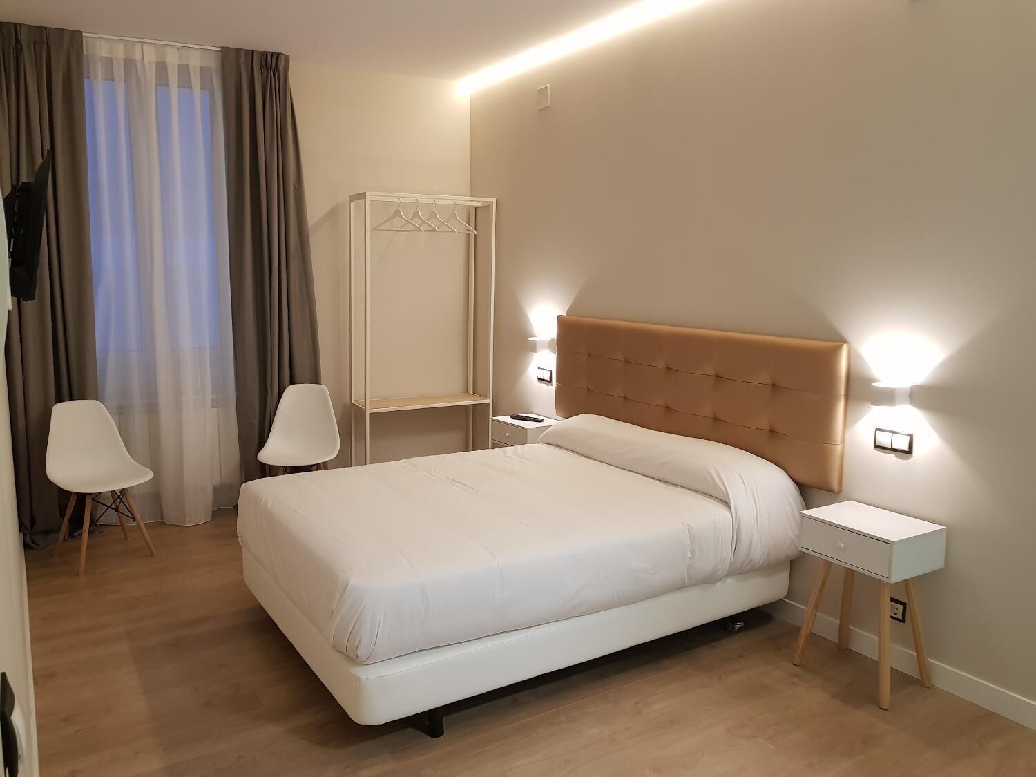 A modern hotel room with a large bed, bedside tables, a wardrobe, and a seating area.