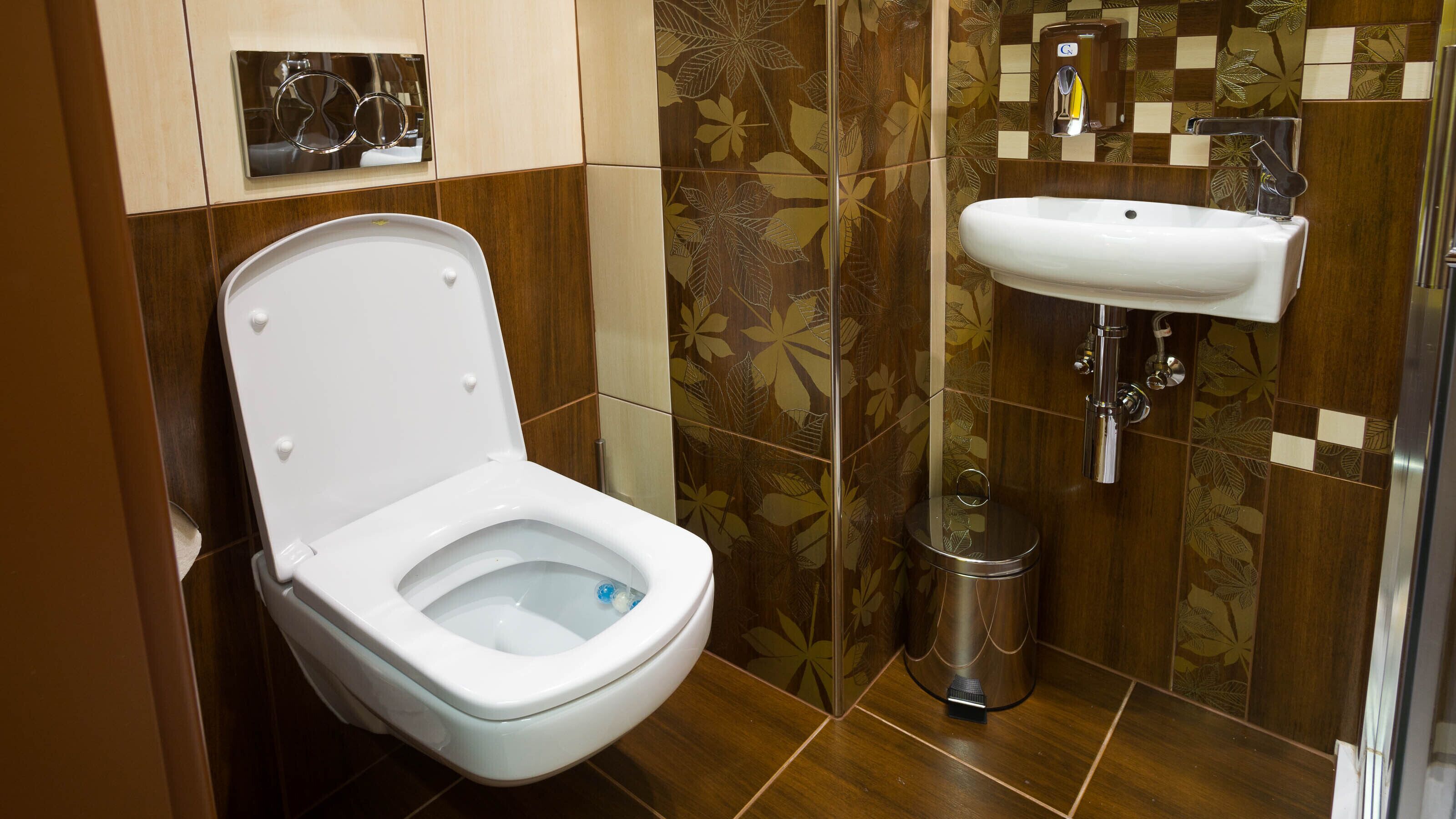 Un baño moderno con inodoro blanco, lavamanos y un cubo de basura.