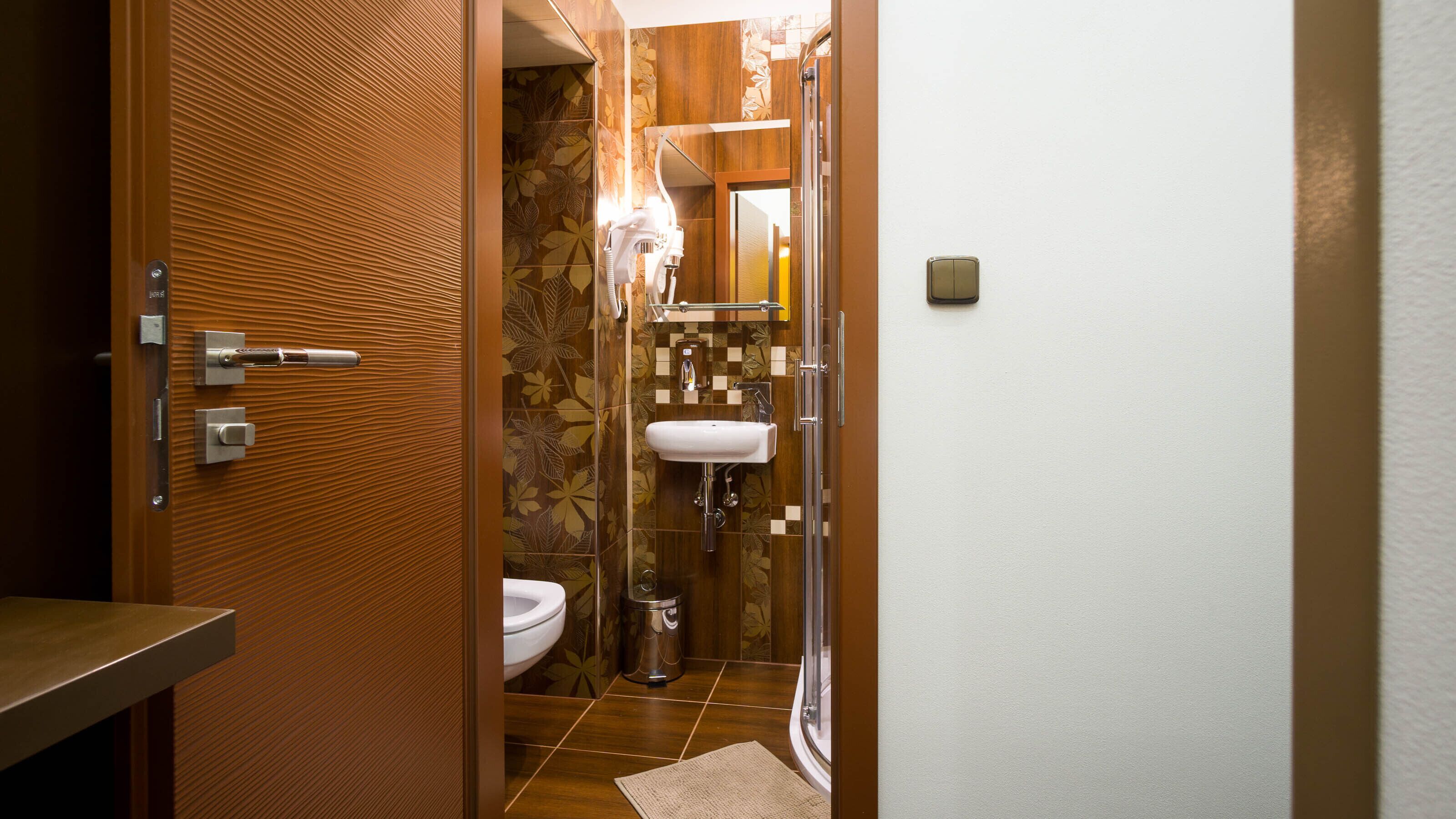 A bathroom with a wooden door, a toilet, a sink, and a shower.