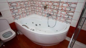 A bathroom with a large bathtub, a toilet, and a shower area.