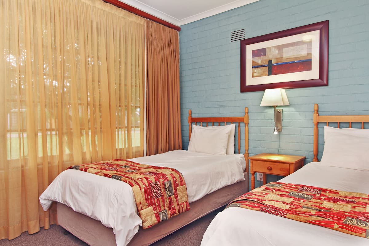A hotel room with two beds, a nightstand, a lamp, and a framed picture on the wall.