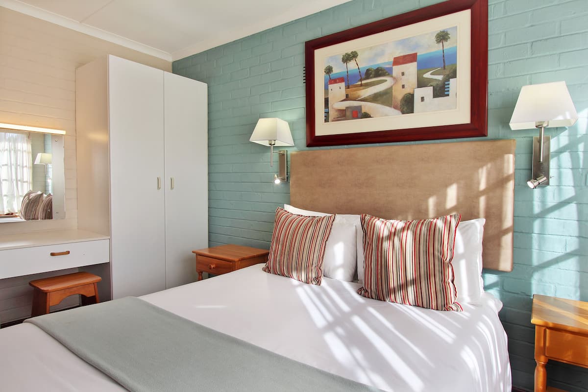 A bedroom with a bed, a nightstand, a dresser, and a painting on the wall.