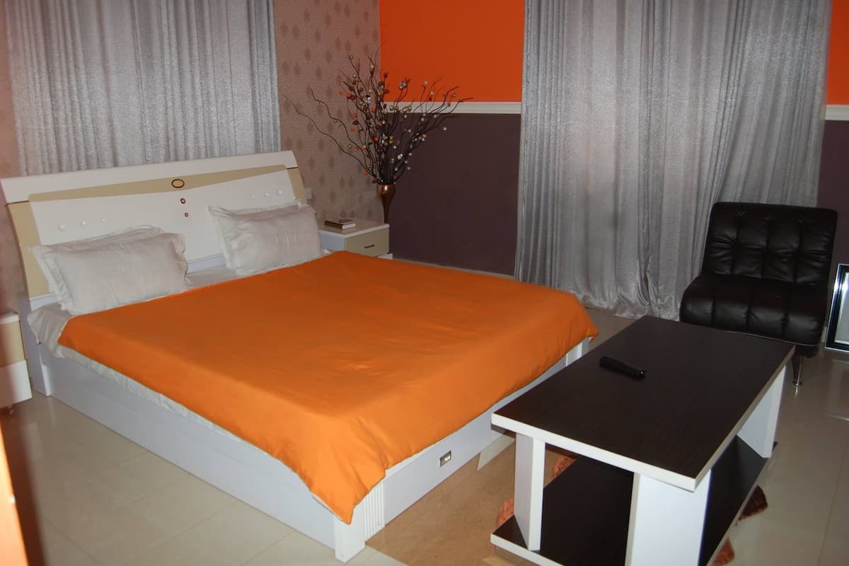 A bedroom with a bed, a bedside table, a chair, and a vase with branches.
