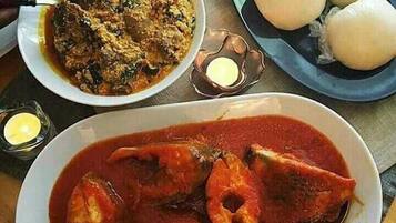 A plate of fish in a red sauce, a bowl of rice with vegetables, and a plate of boiled eggs.