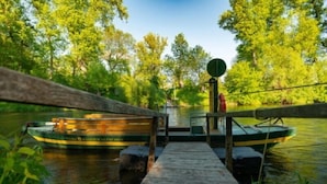 Eine hölzerne Anlegestelle führt zu einem grünen Boot mit der Aufschrift 'WATERFRONT', das an einem ruhigen Fluss inmitten üppiger Vegetation liegt.
