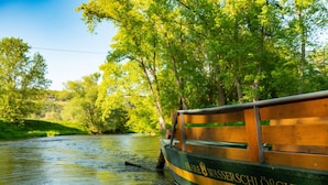 Ein Boot mit dem Namen "Fährwasserschlöbchen" auf der Seite, das auf einem Fluss zwischen üppigem Grün treibt.