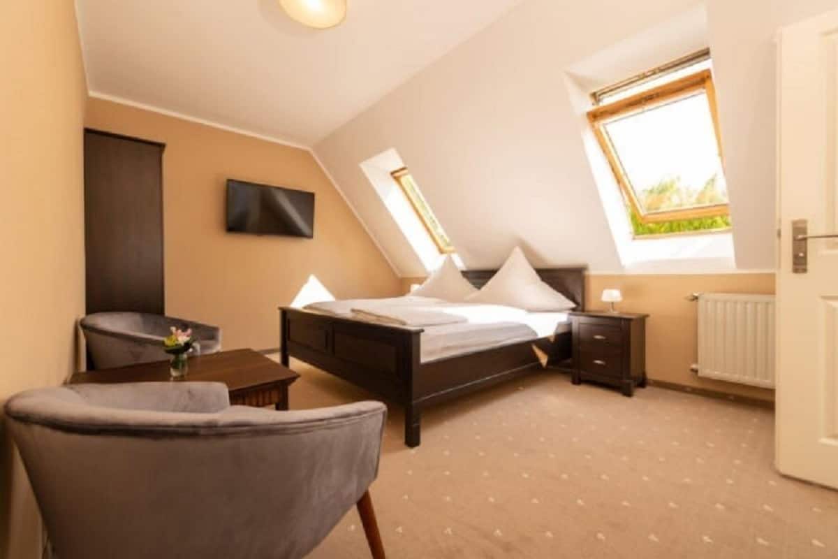 Een slaapkamer met een bed, nachtkastje, stoel en een raam met uitzicht.