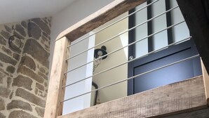 Eine rustikale Holztreppe führt zu einem Schlafzimmer mit einer Steinsäule und einem Fenster mit Metallgitter.