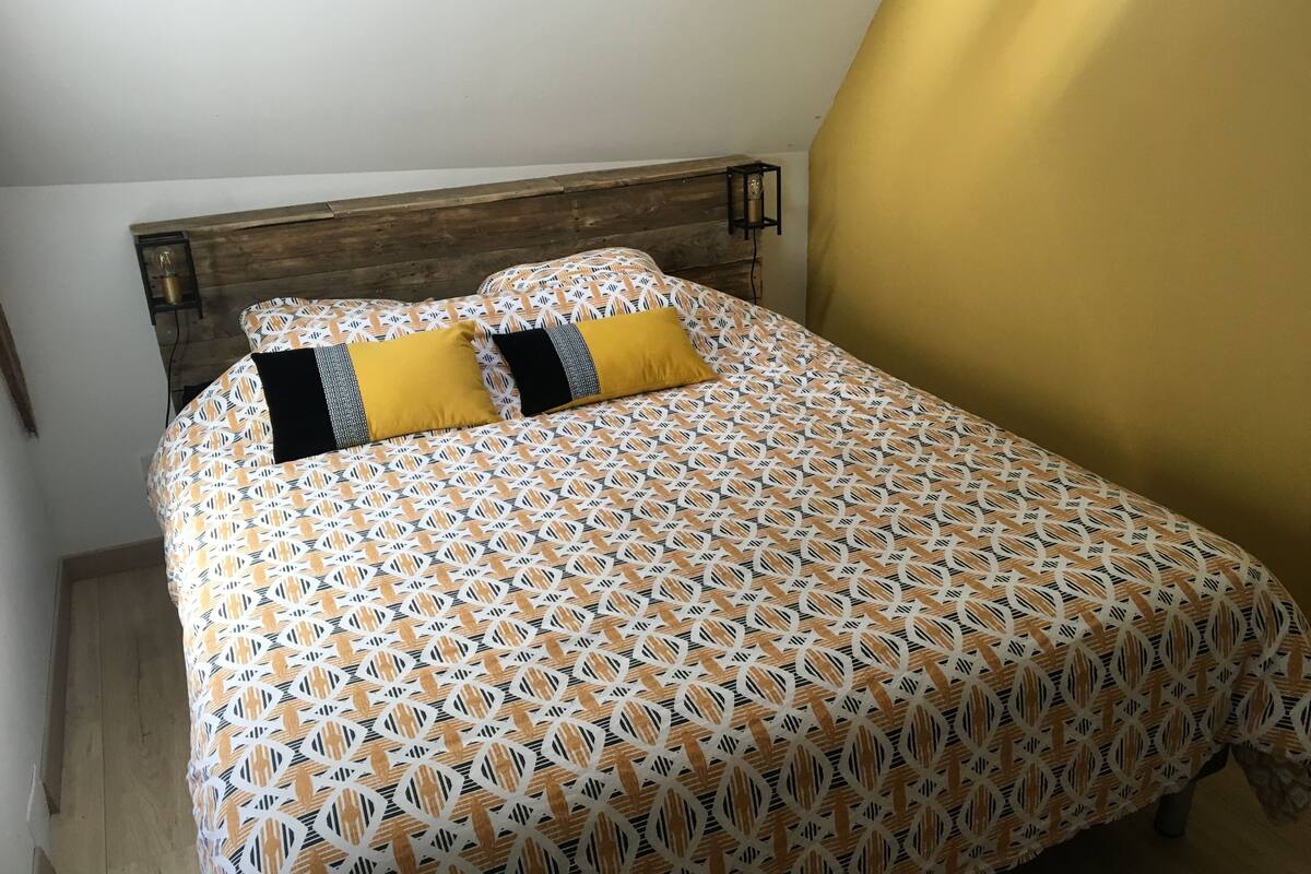 Un lit avec une couvre-lit à motifs, deux oreillers et une tête de lit en bois.