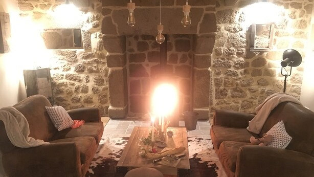Ein gemütliches Wohnzimmer mit Steinwänden, zwei Ledersofas, einem Holztisch und einem Steinkamin.