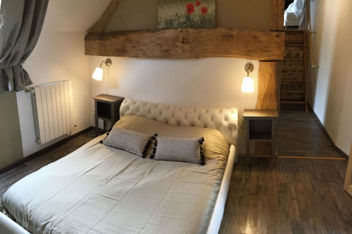 Une chambre à coucher avec un grand lit, des poutres en bois, deux tables de chevet et un radiateur.