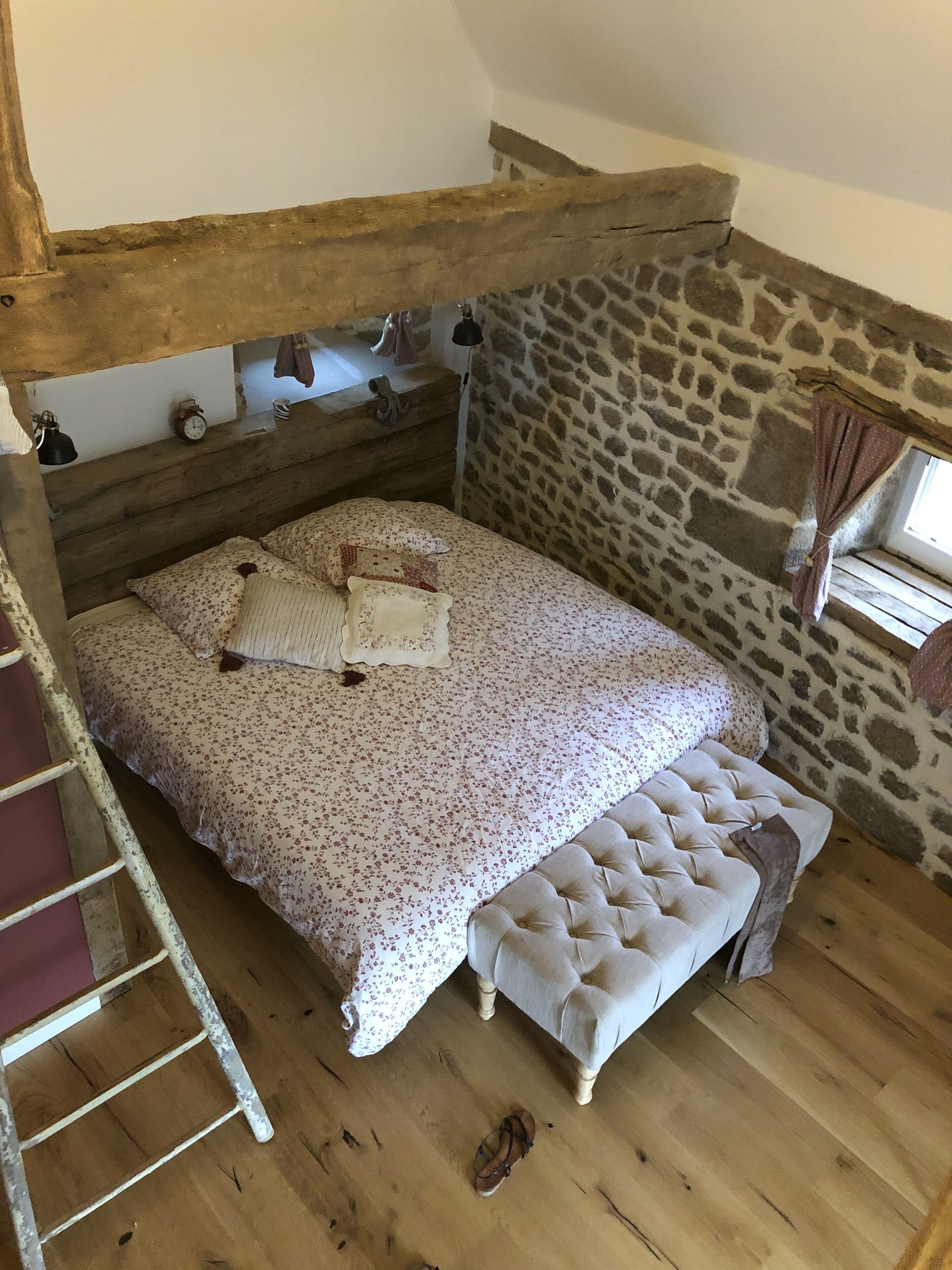 Un dormitorio rústico con literas de madera, una pared de piedra y una pequeña ventana con cortinas.