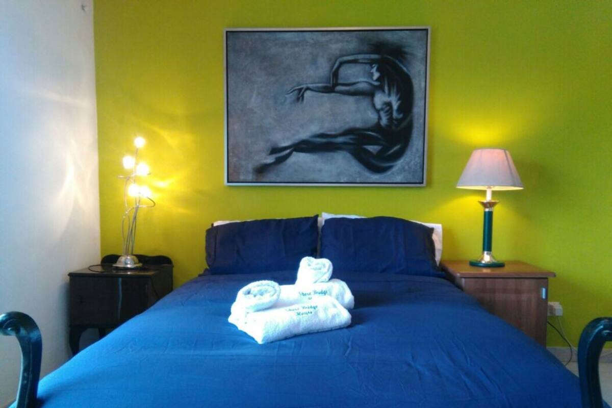 A bed with a blue bedspread, a folded towel, and a painting on the wall.