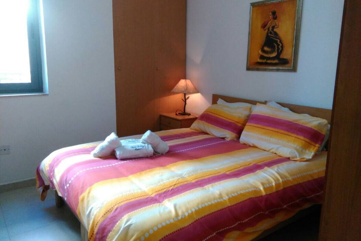 A neatly made bed with striped bedding, a bedside lamp, and a painting on the wall.