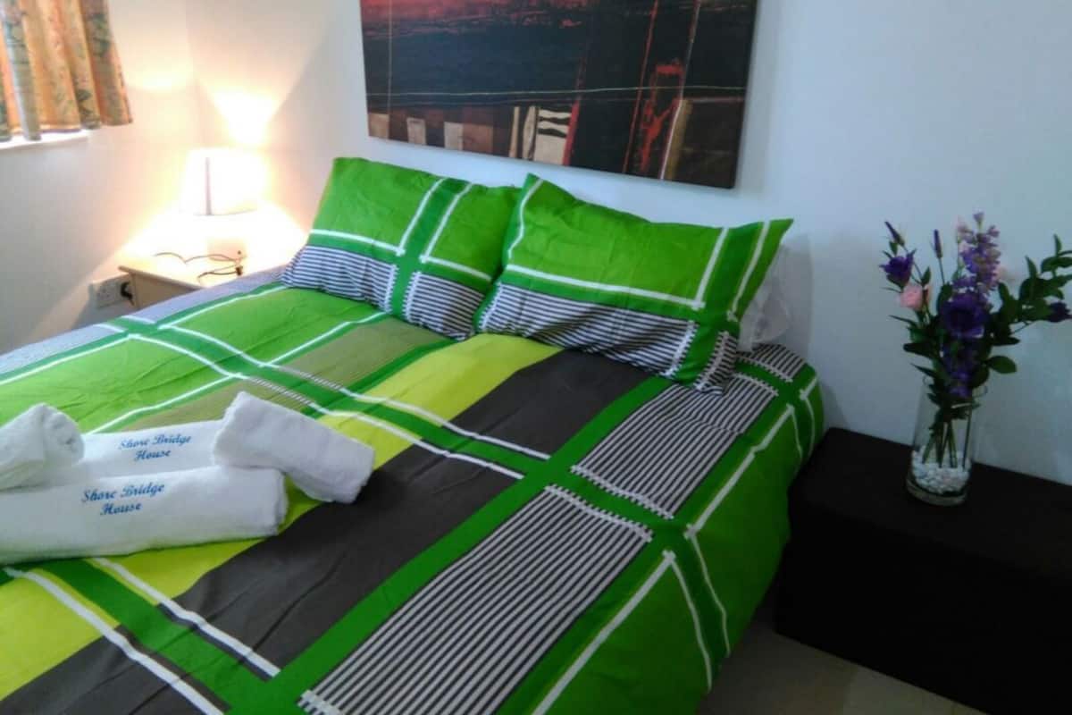A neatly made bed with green and white bedding, a bedside lamp, and a vase with flowers on a nightstand.