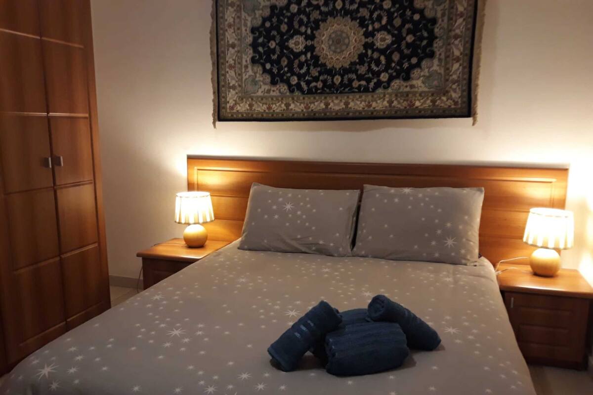 A neatly made bed with a star-patterned bedspread, two pillows, and two bedside lamps.