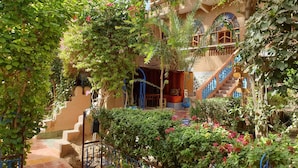 Un edificio tradicional con una escalera que lleva a un balcón, rodeado de abundante vegetación y plantas con flores.