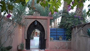 Un arco decorativo que da acceso a un patio con suelo de baldosas y plantas en macetas.