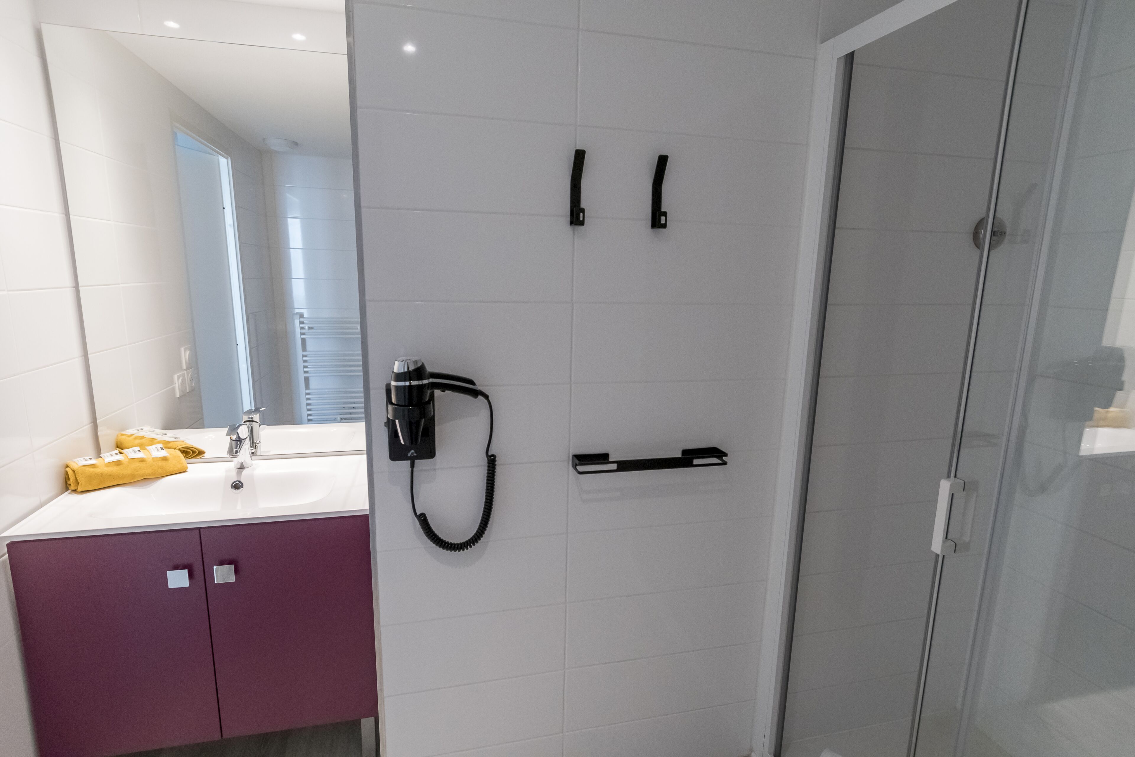 Un bagno moderno con un lavandino bianco, mobiletti viola, cabina doccia in vetro e porta asciugamani.