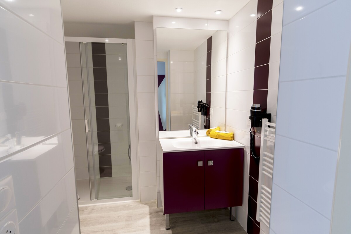 A modern bathroom with a glass shower enclosure, a white sink with a purple vanity, and a towel rack with a yellow towel.