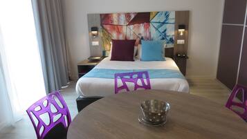 Una habitación de hotel con una cama, una mesa y sillas moradas. Hay un cuadro en la pared detrás de la cama.
