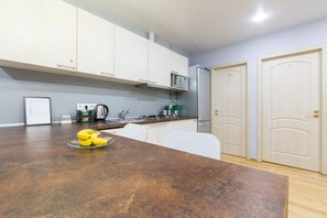 Kitchen area with a stove, microwave, and kettle, featuring a sink and white cabinets.