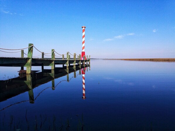 A calm water body with a wooden pier and a red and white striped lighthouse. - Lagoa Country Club (Cidreira)