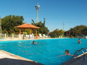 A swimming pool with people swimming, a gazebo, and lounge chairs. - Lagoa Country Club (Cidreira)