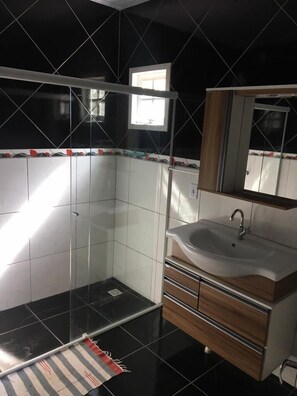 A modern bathroom with a glass shower enclosure, a sink with a wooden vanity, and a mirror above the sink. - Lagoa Country Club (Cidreira)