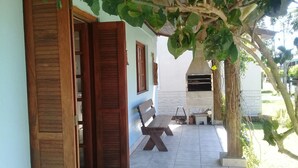 An open wooden door leading to a covered patio area with a bench and a grill. - Lagoa Country Club (Cidreira)