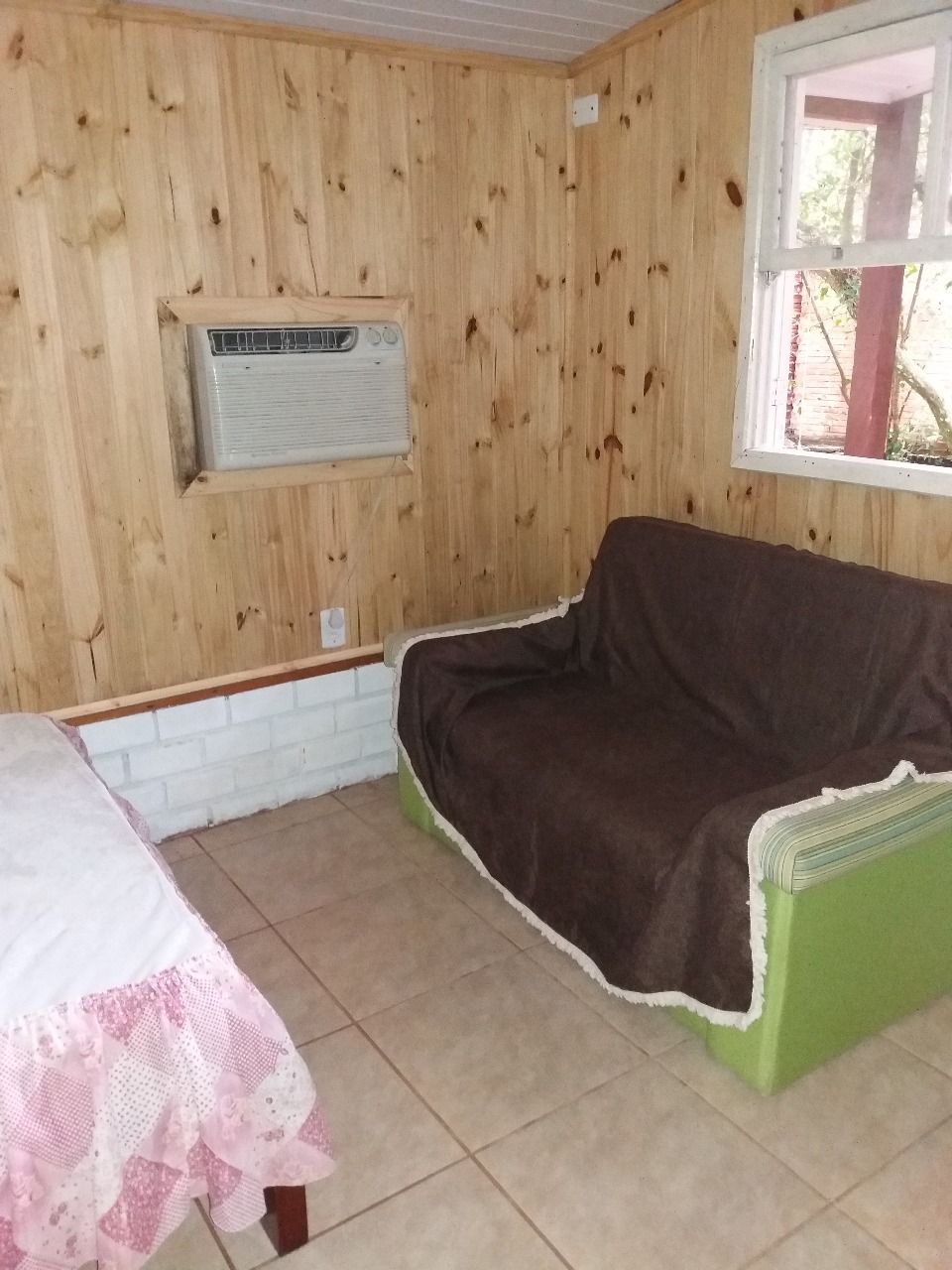 A room with a wooden wall, a window, a green sofa, and a white table with a pink tablecloth.