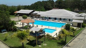 A pool area with a large rectangular pool, lounge chairs, and a covered seating area. - Lagoa Country Club (Cidreira)