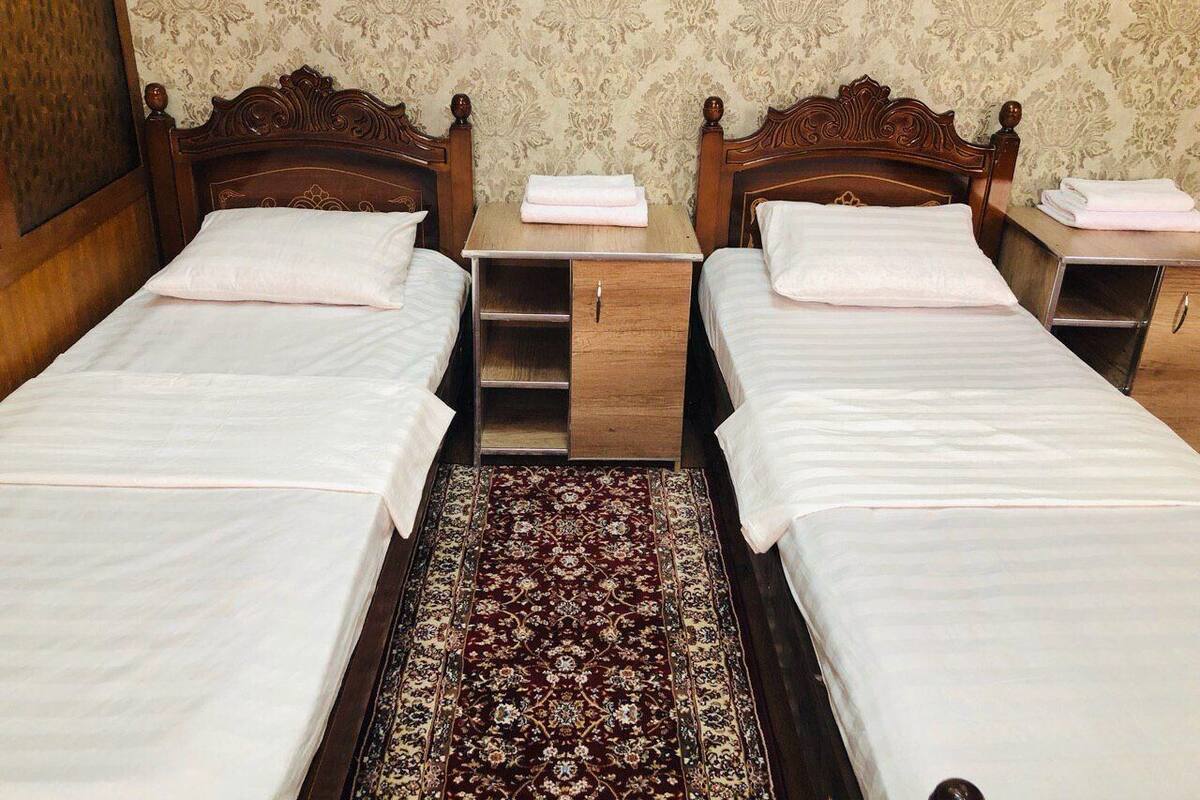 Ein Hotelzimmer mit zwei Einzelbetten, Holzkopfteilen, einem kleinen Nachttisch mit Lampe und einem gemusterten Teppich.